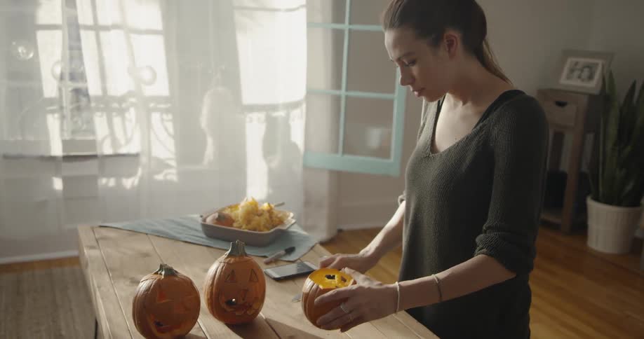 A woman carves pumpkins on a kitchen table