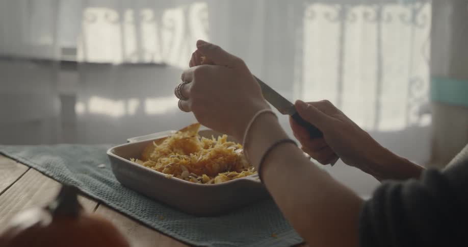 A woman is cutting pumpkin into a baking dish