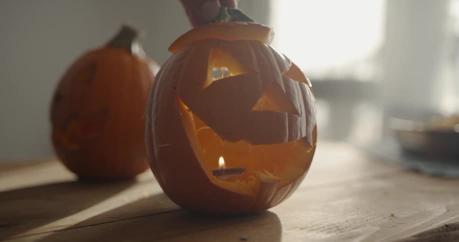 A person places a candle inside a carved pumpkin