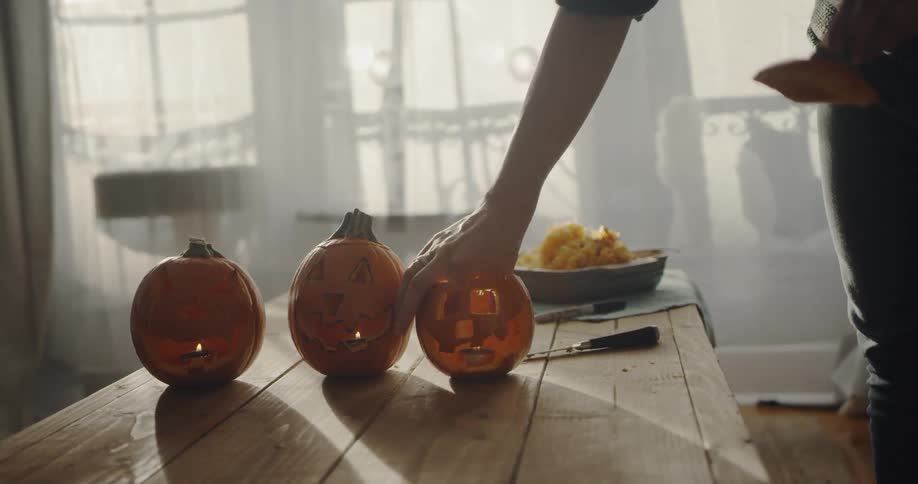 A woman places a candle in a third jack o lantern