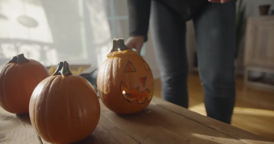 A woman arranges jack o lanterns on a table and cleans up