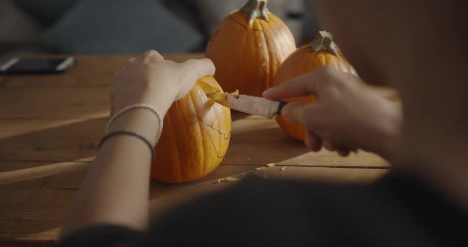 A woman carves eyes on a pumpkin using a knife