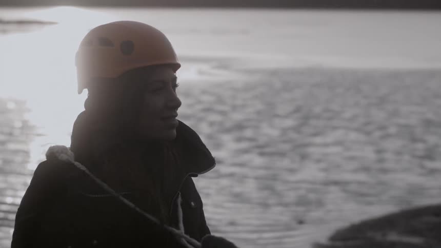 A woman wears a hardhat next to a lake while it snows