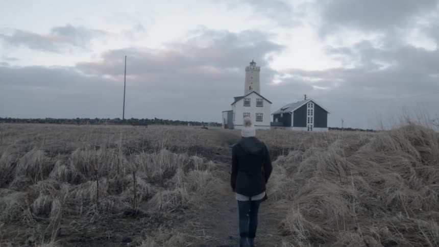 A woman walks towards a rural building at sunset