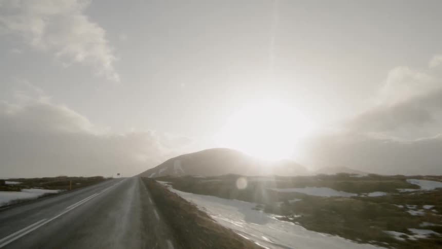 A vehicle drives down a rural road towards mountains