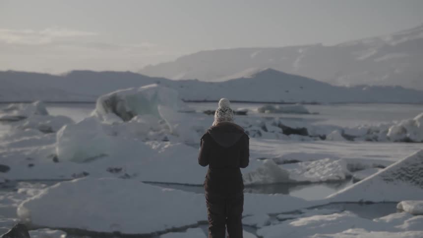 A woman is standing and looking at icebergs during the day