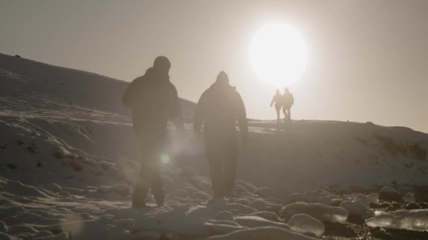 Hikers walk in snowy mountains at sunset