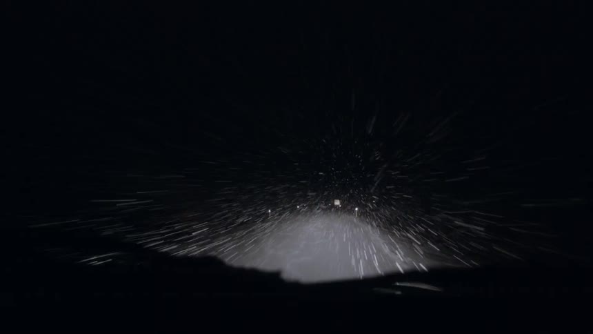 A car is driving down the dark snowy road