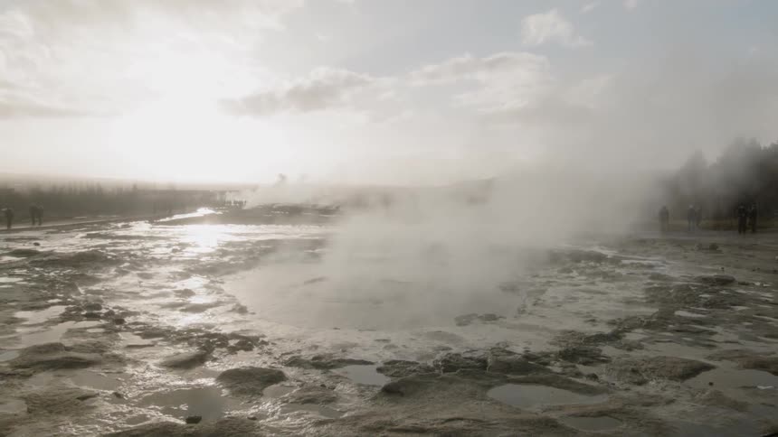 Steam rises up from  a hot spring on a sunny day