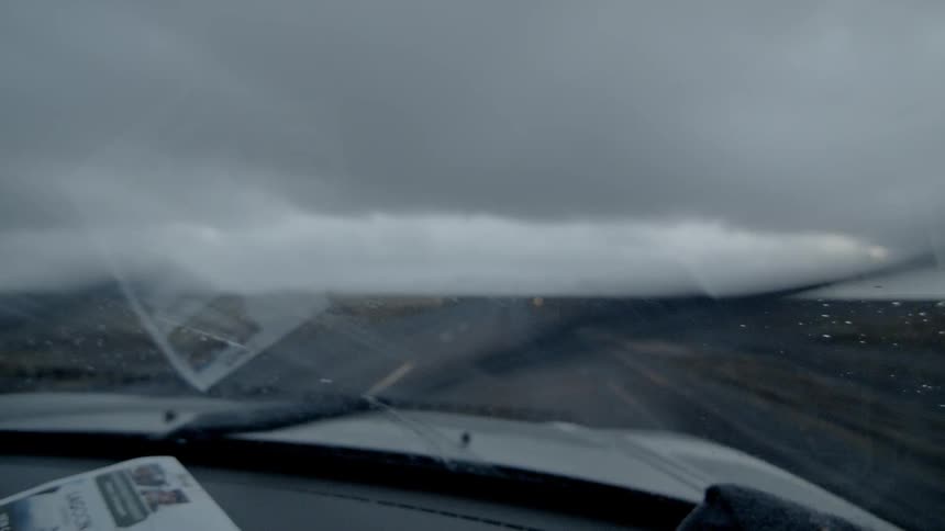 A car is driving down a straight flat road with its windshield wipers on
