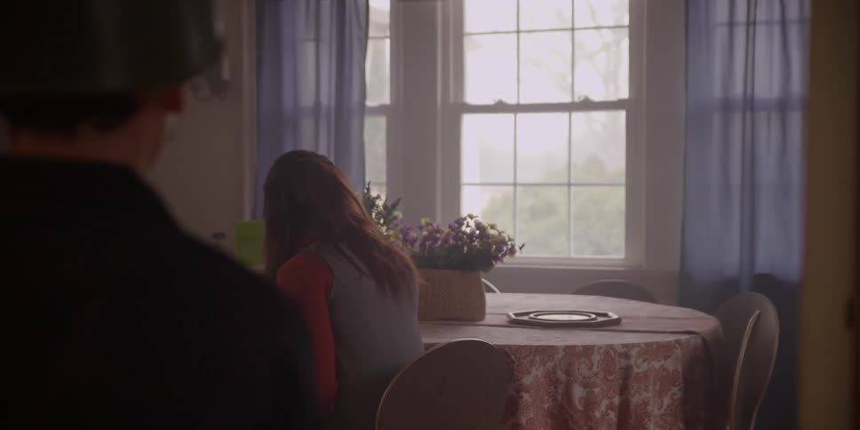 A person in uniform approaches a woman sitting at a dining room table