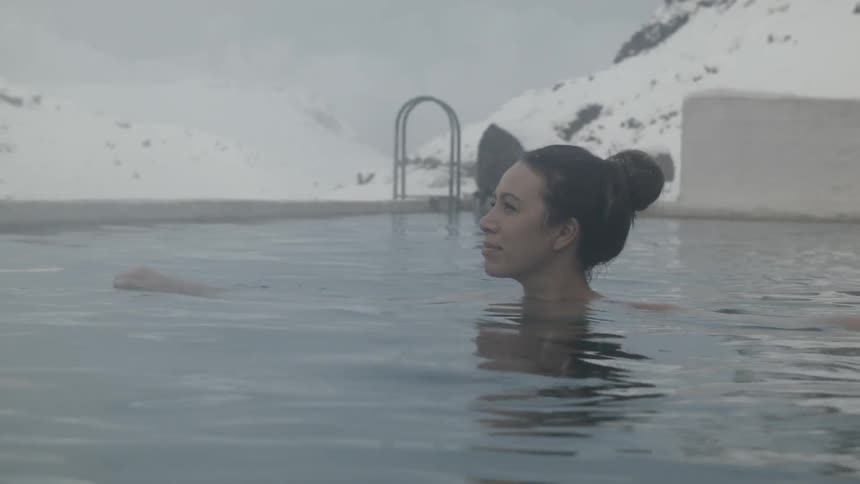 Woman stands in an outside pool with snowy mountains behind