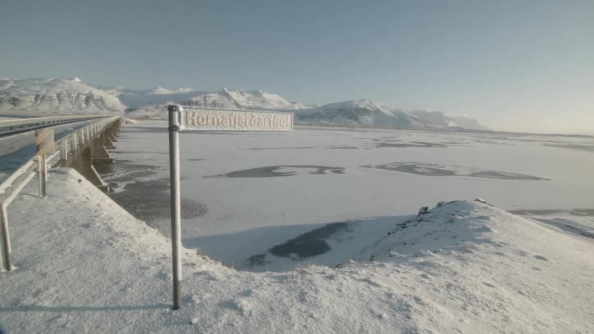 A frozen sign marks a frozen river next to a highway