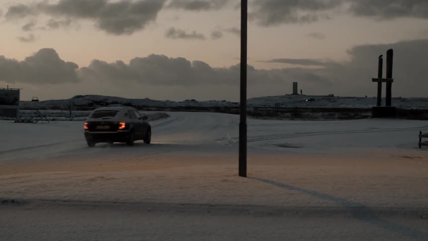 A car is traveling down a snow covered road at sunset