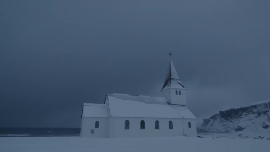 An ocean side church is covered in snow on a cloudy day