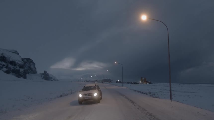 A car is driving down a snow covered road at night
