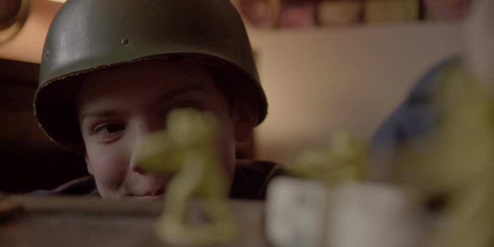 Boy wearing army helmet has fun playing with toy soldiers