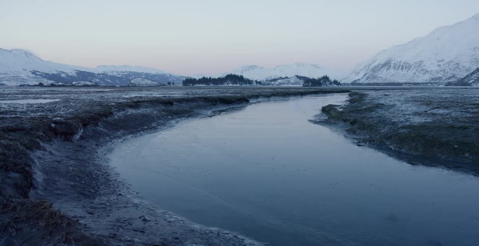 A river is flowing through a mountain valley at dawn in winter