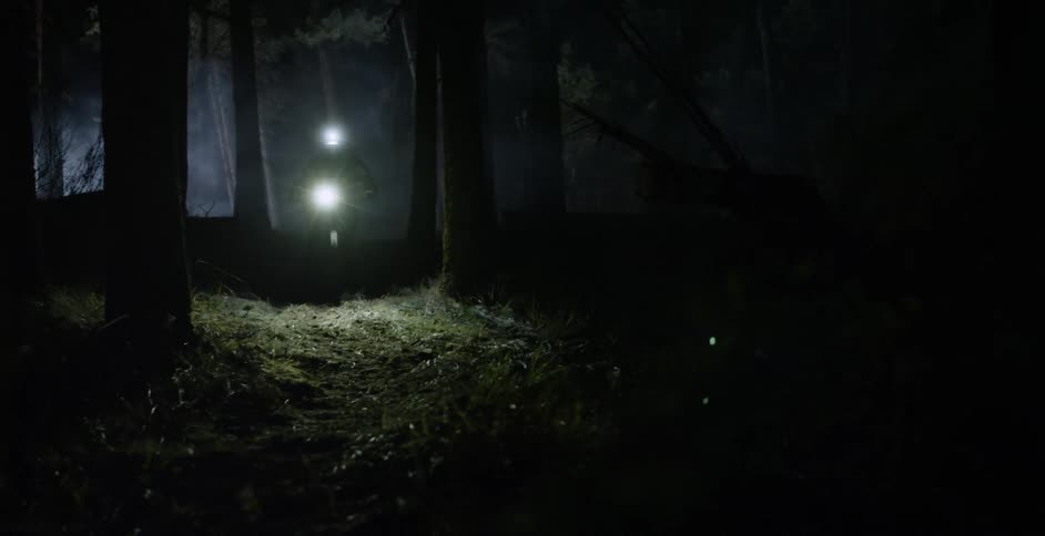 A man rides a bike through the woods with lights on his helmet and bike