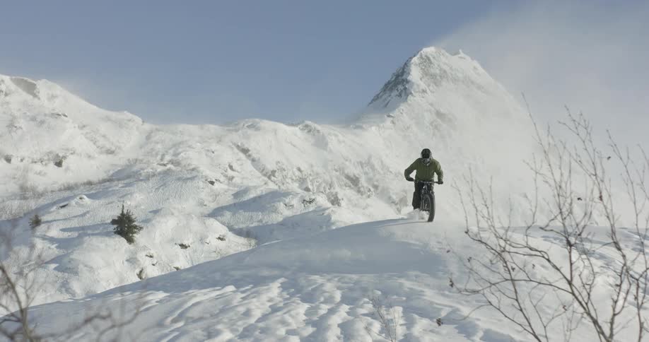 A person rides a mountain bike down a snow covered slope