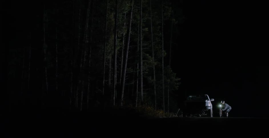 A person puts his bicycle in the truck at night
