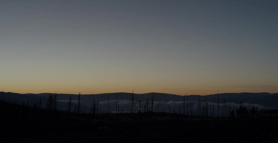 The sky darkens as the sun sets over mountains