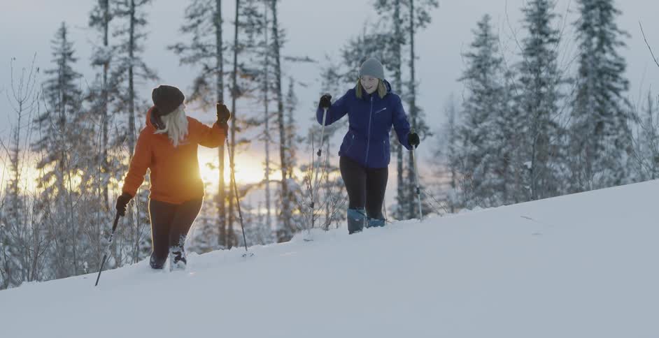 Two women hike slowly through the tall snow