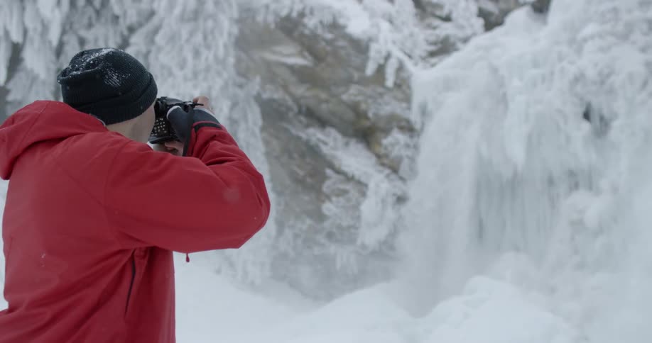 A man photographs a snowy waterfall