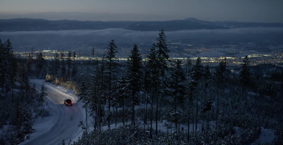 A truck drives through a snowy forest at dusk