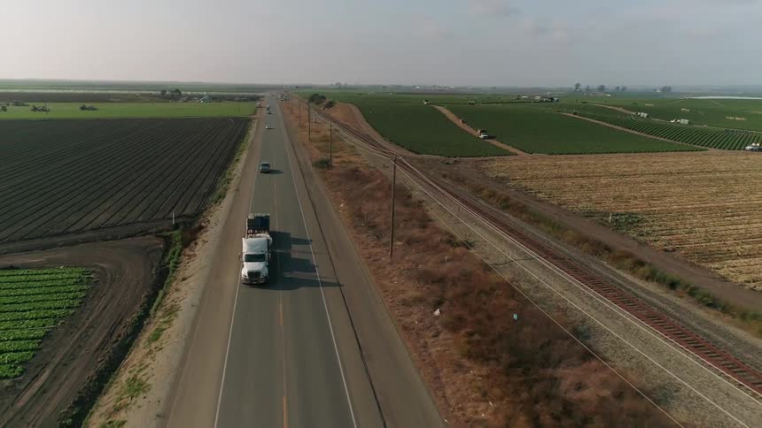 A truck hauls equipment on a road next to farmland
