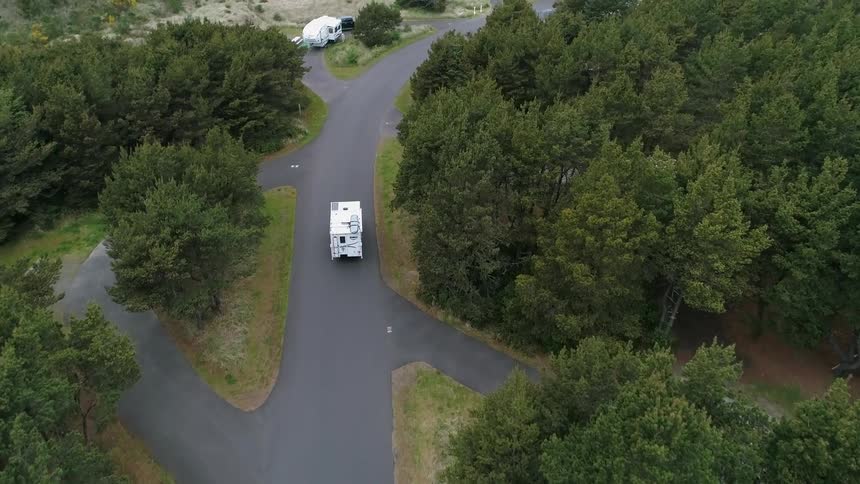 A camper trailer is being driven into a campgrounds in a natural setting during the day