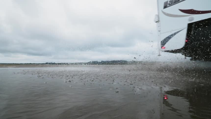 A truck hauling a camper rides through a puddle