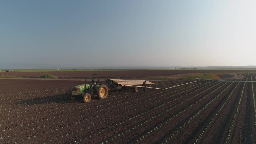 A tractor pulls farming supplies across a crop field