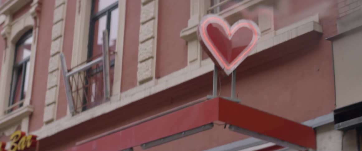 A sign with a neon heart shines above a shop on a city street during the day
