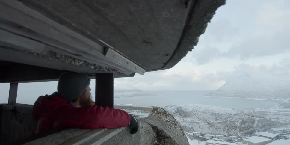A man looks out from a lookout tower onto a snowy village