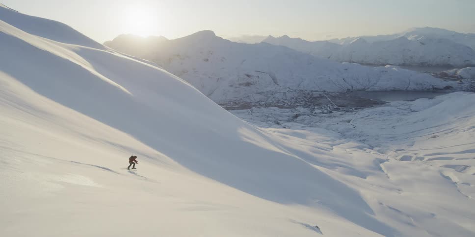 A skier turns down a snowy mountainside at sunset
