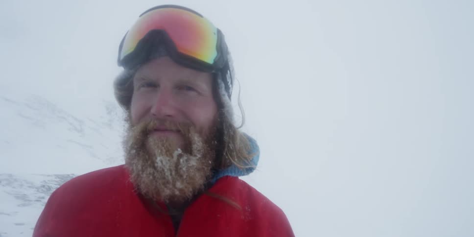 A man wearing snow goggles smiles outside in the snow