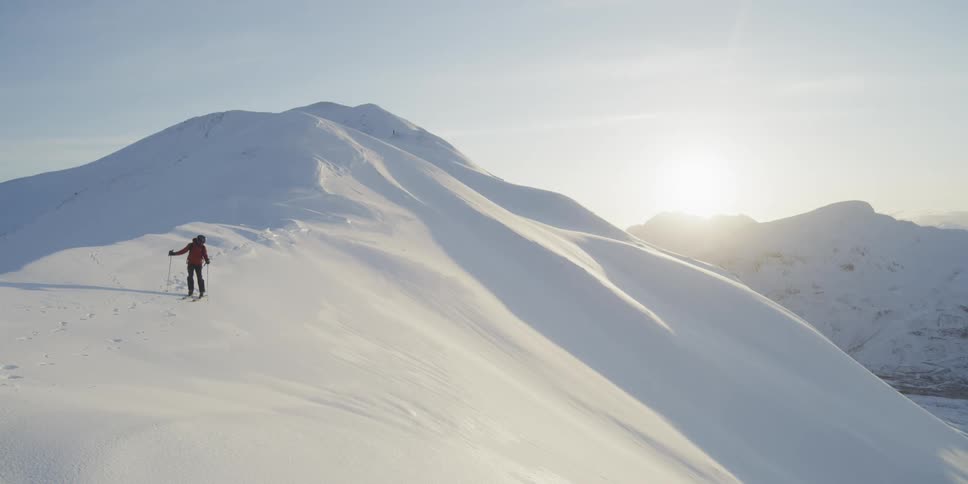 A skier stands on a snowy mountain at sunset