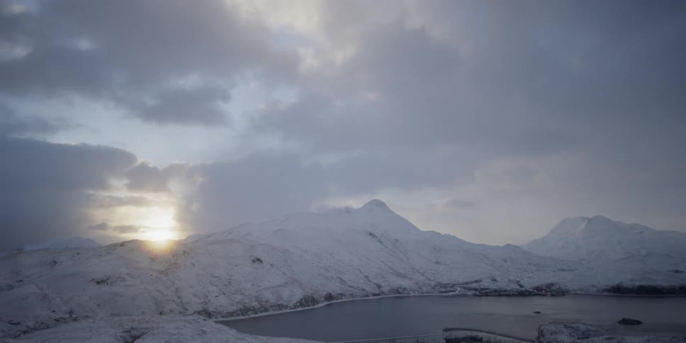 Time-lapse of clouds moving over snowy mountains at sunset