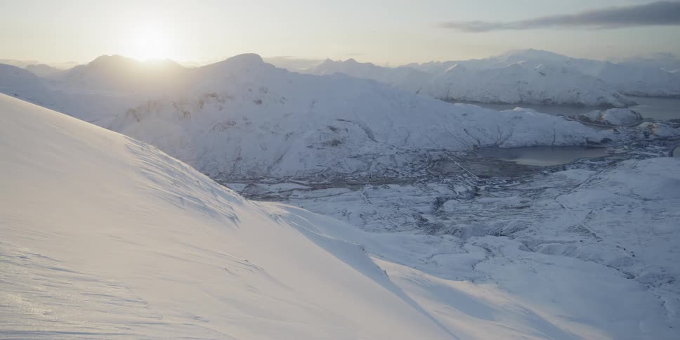 The sun is rising over a snow covered mountain valley and coastline