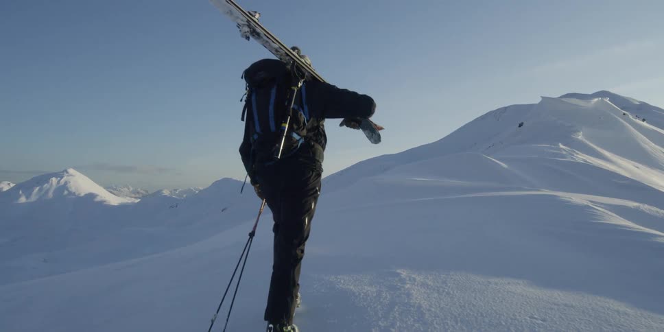 Two skiers hike up a snowy hill with their dog