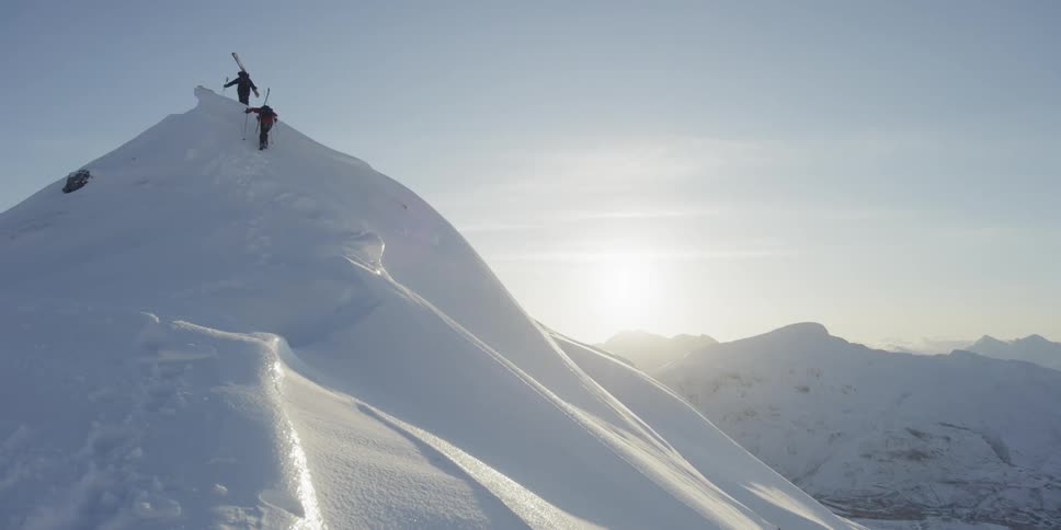 Skiers hike up a snowy mountain at sunset