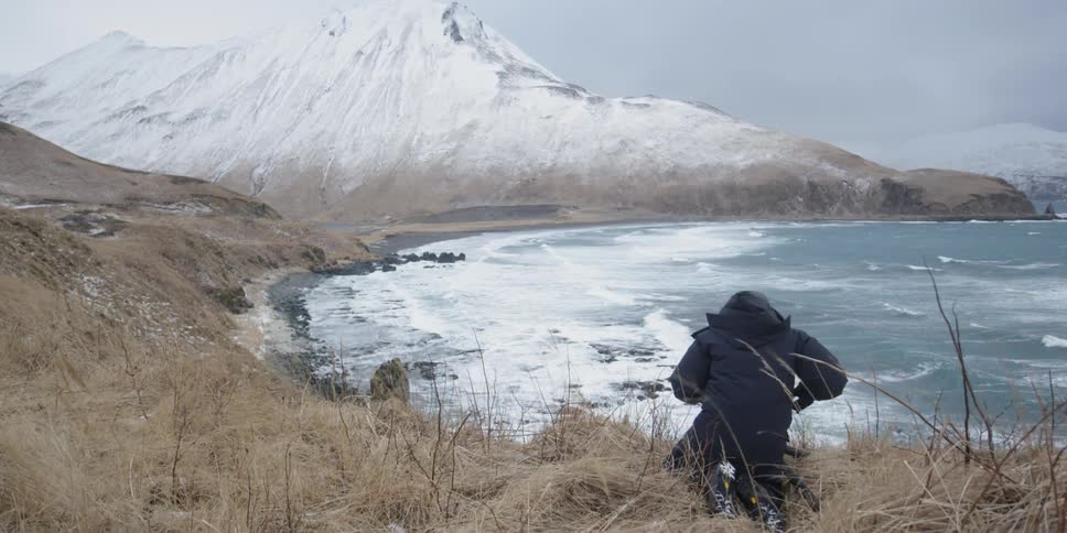 A man in a jacket takes pictures of an icy beach