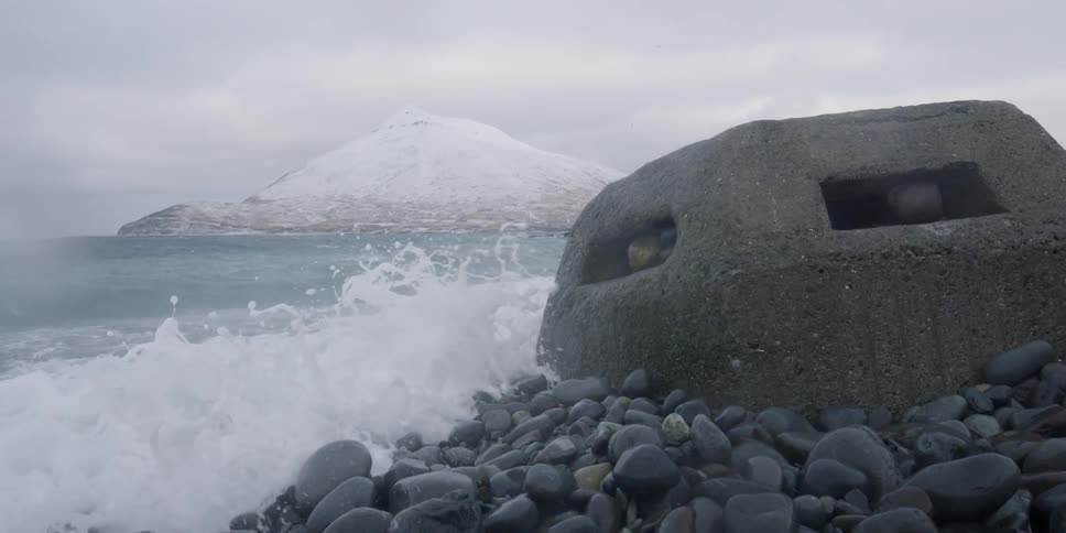 Waves are crashing over rocks and a bunker on a beach in winter