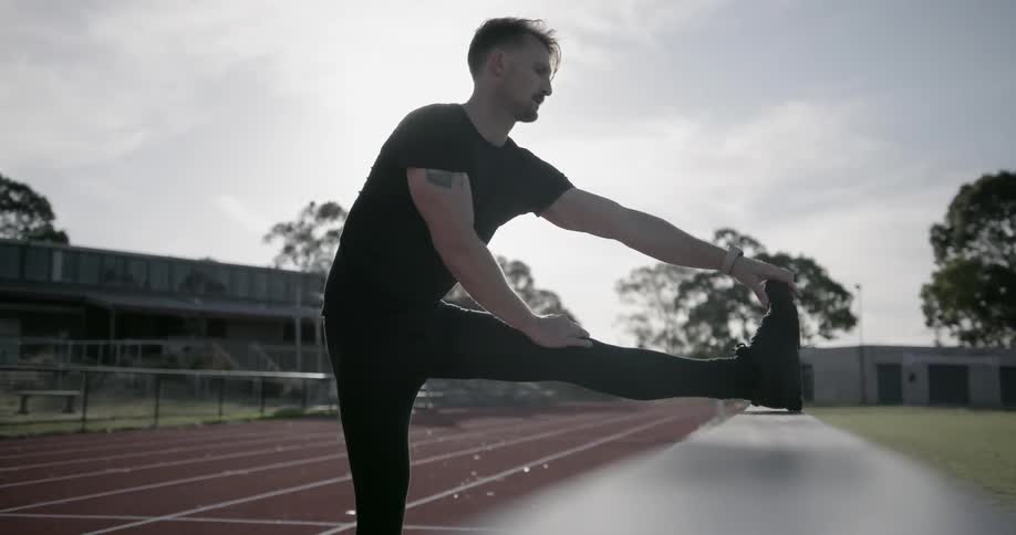 A man stretches on the railing of a running track