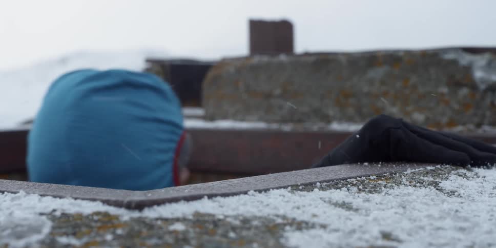 A man in a red coat exits a lookout building in the snow
