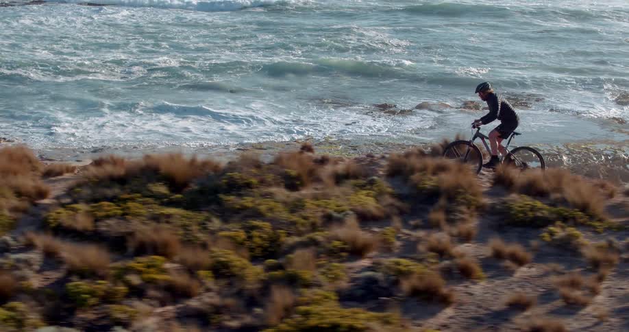 Man rides a bike over a bumpy path near the ocean