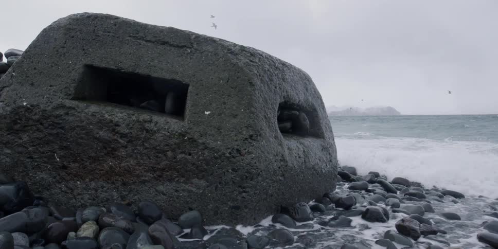 A concrete bunker sits on rocks as waves come to shore