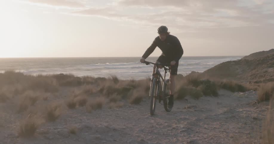 A bicyclist rides on an ocean coast at sunset