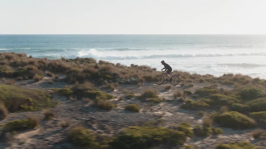 A man is riding his bicycle near the water uphill